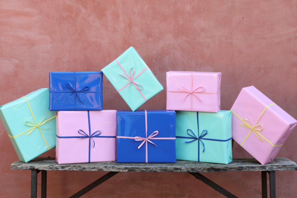 Billede af en gavebunke med lyserøde, blå og grønne gaver på et bord.