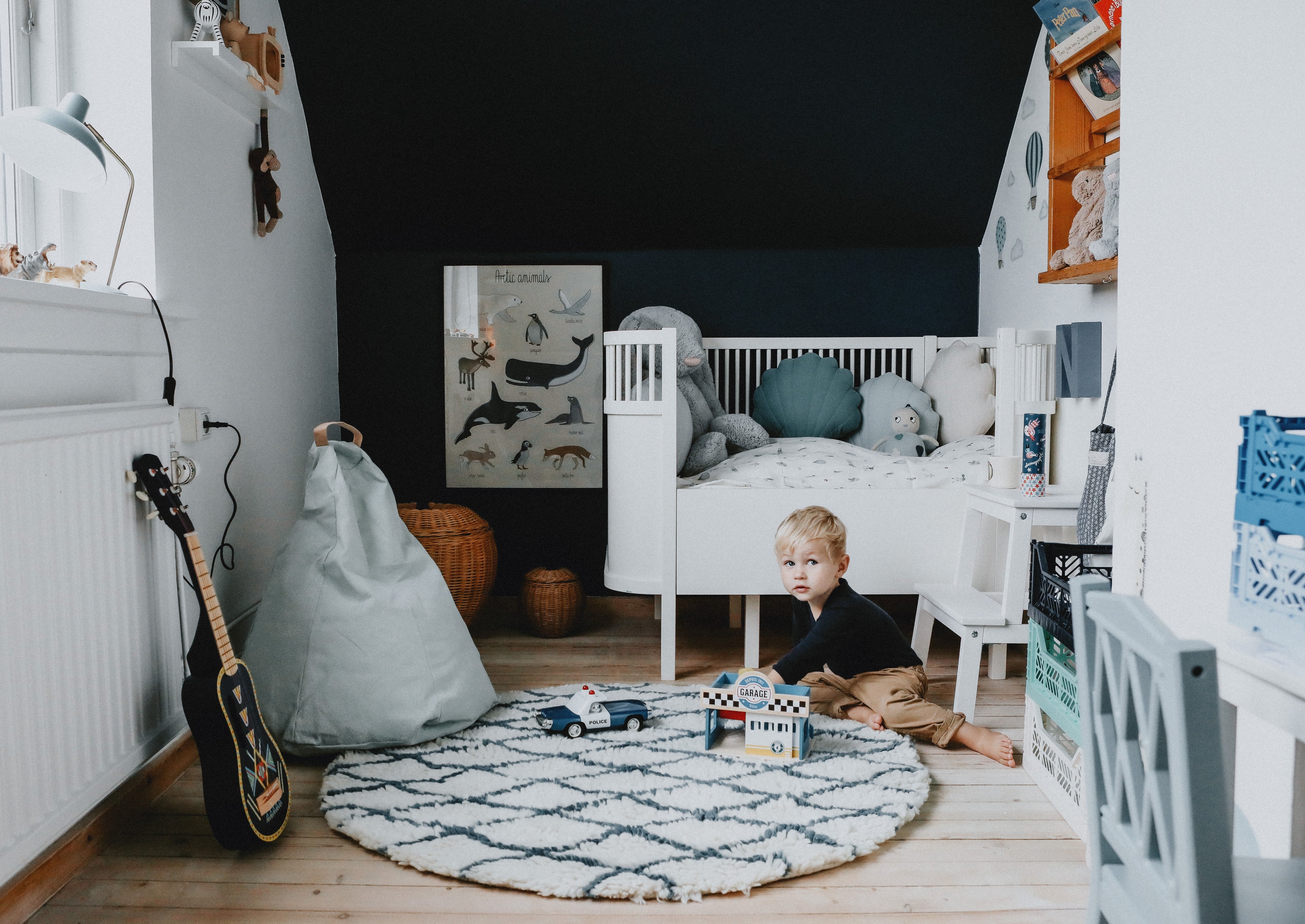 Barn leger på tæppe foran seng med garage og politibil.