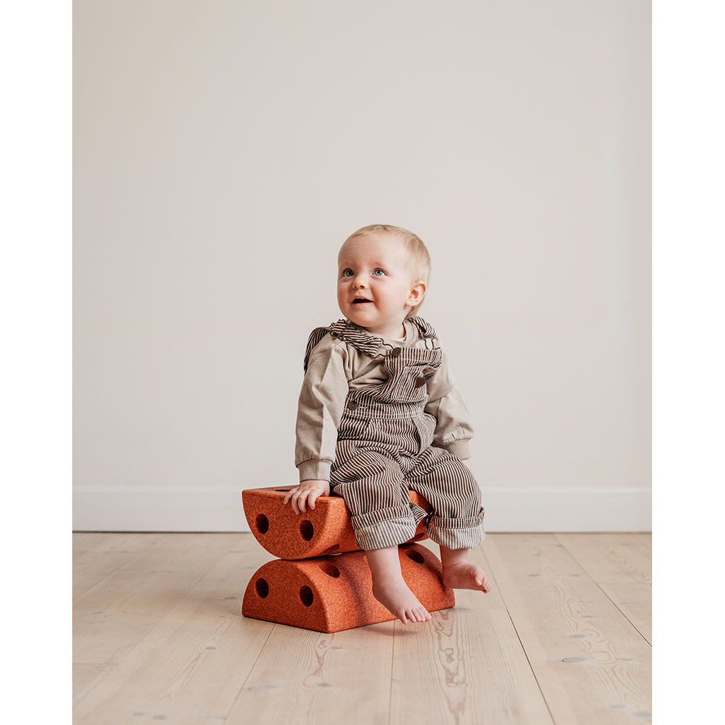 Baby sidder på to brændt orange Modu skamler på trægulv.